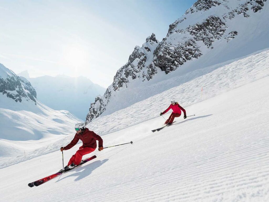 2 Skifahrer in roter Kleidung rasen die Piste hinunter in Lech