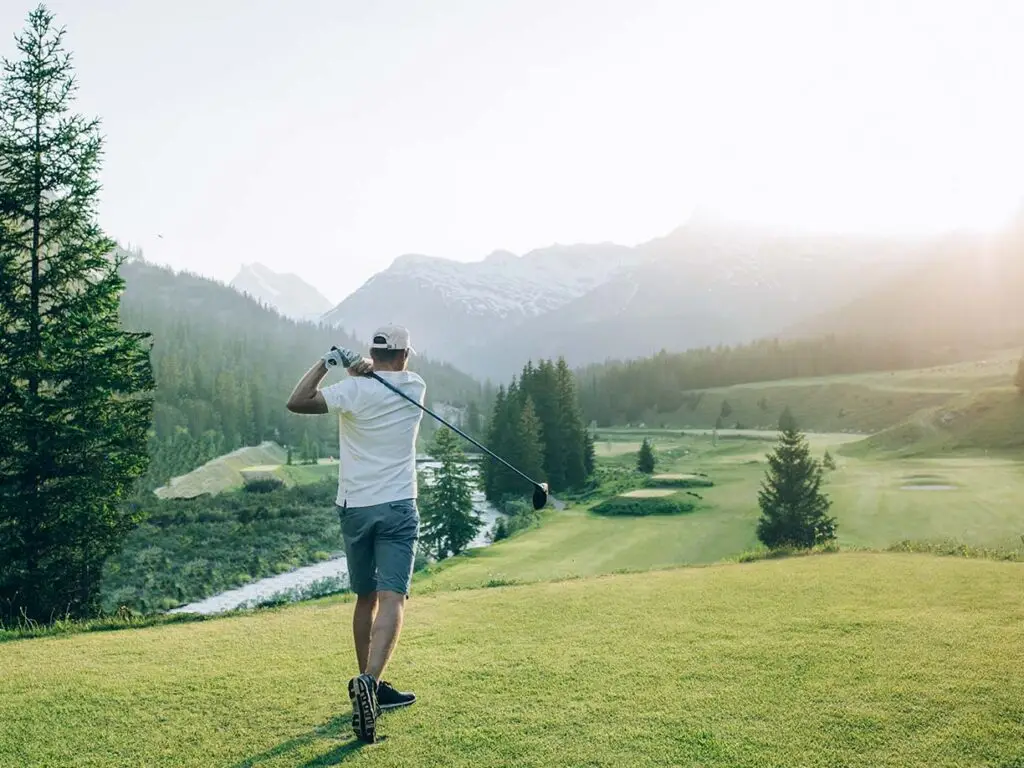 Mann mit Golfausrüstung auf dem Golfplatz in Lech, zwischen grünen Wiesen und Bäumen