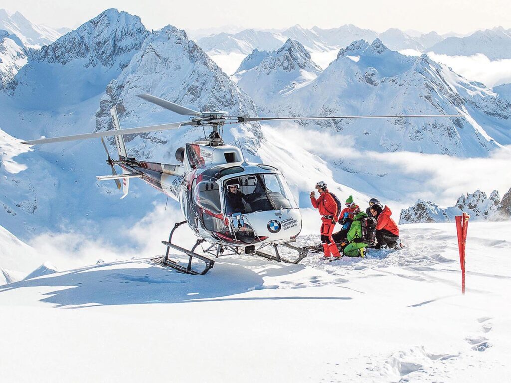 Skifahrer-Gruppe neben Helikopter mitten im Schneegebiet in den Bergen