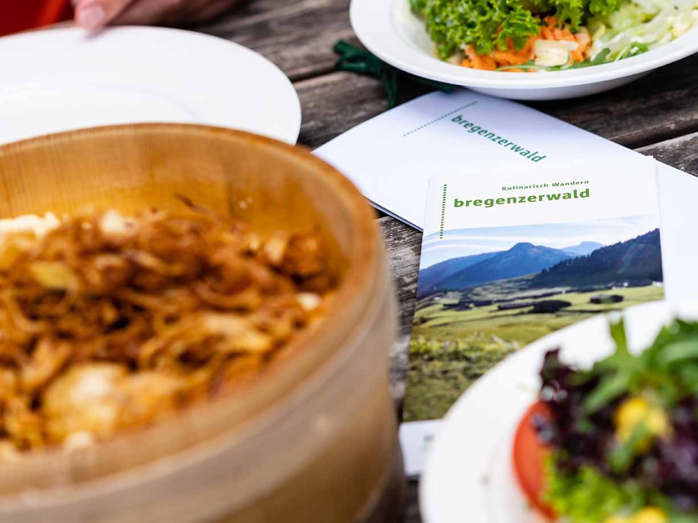 Bregenzerwälder Käsknöpfle und Salat mit Flyer auf Tisch