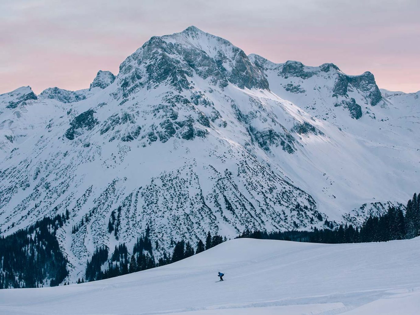 Verschneiter Berg und Abdendrot mit Skifahrer auf der Piste in Lech am Arlberg