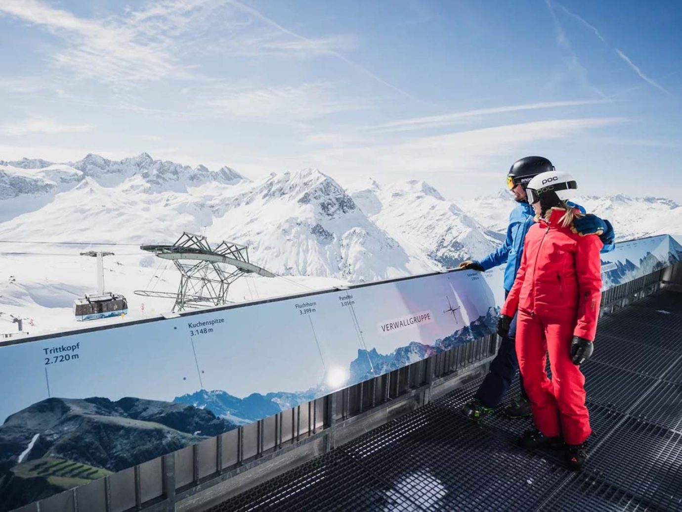 2 Skifahrer bei Aussichtsplattform blicken auf Seilbahn